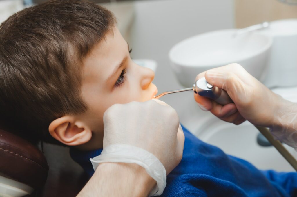 Pediatric dentist treats child caries and oral cavity of boy sitting in dentist chair during regular